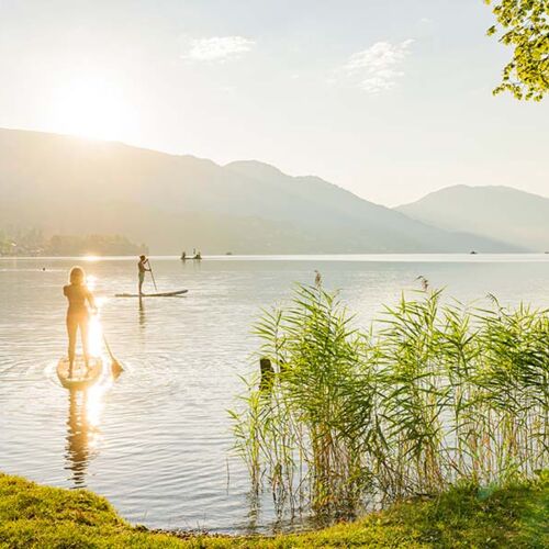 Lake Millstatt in Carinthia, surrounded by mountains. In the lake people have fun swimming and stand-up paddling